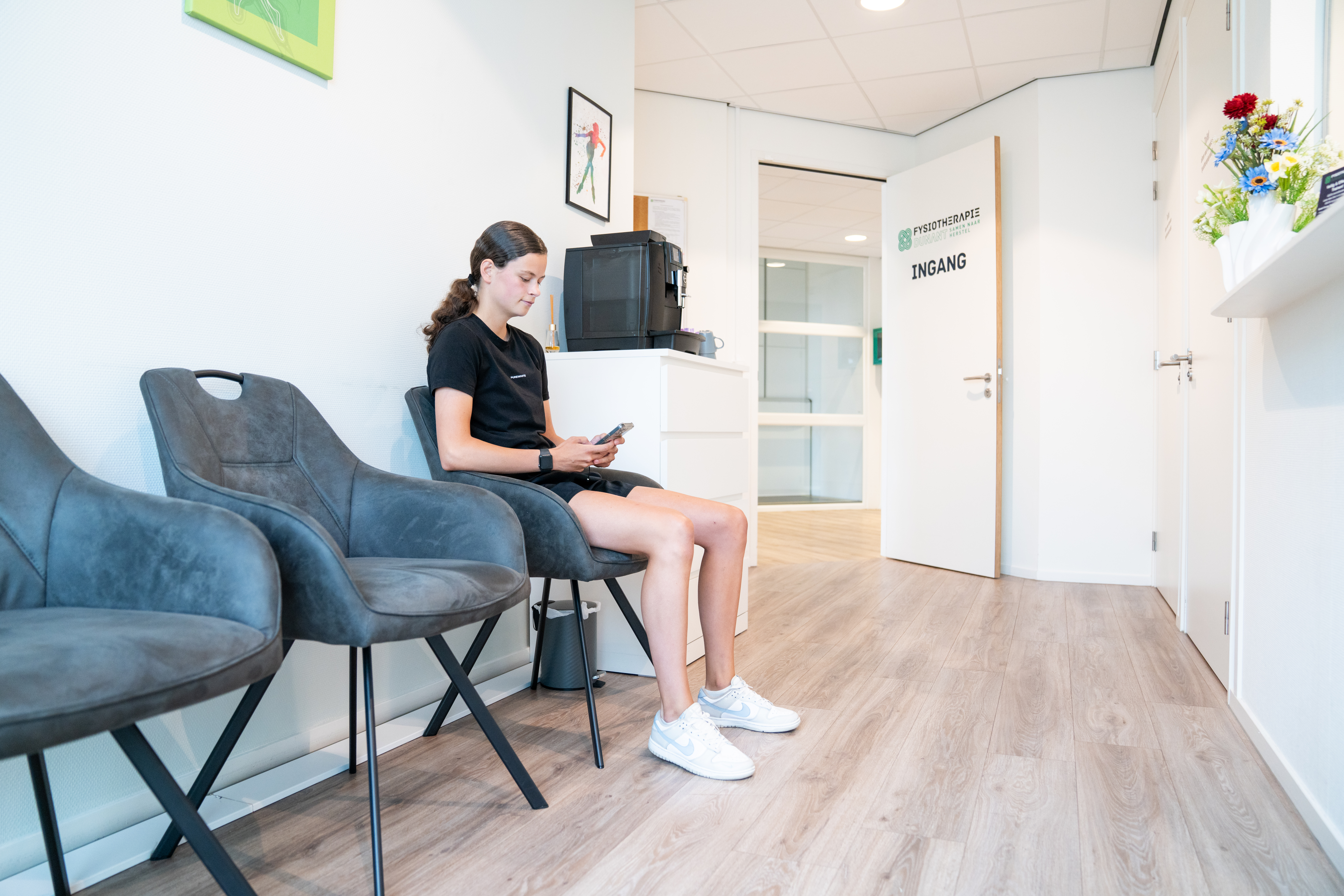 Vrouw in de wachtruimte van Fysiotherapie Dunant kijkt op haar mobiele telefoon