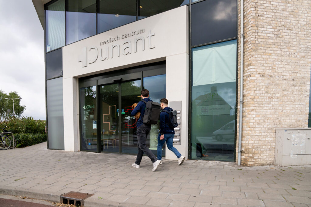 Twee fysiotherapeuten lopen de praktijk van Fysiotherapie Dunant in Roosendaal binnen.