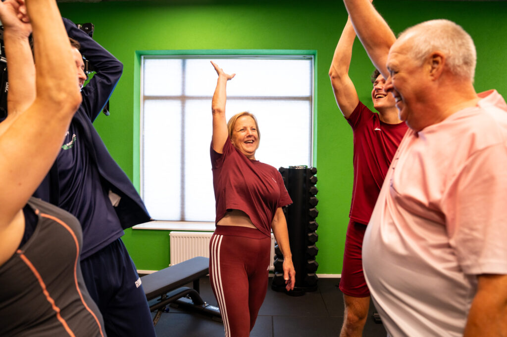 Deelnemers doen schouder- en rekoefeningen met de armen omhoog onder begeleiding bij Fysiotherapie Dunant in Roosendaal